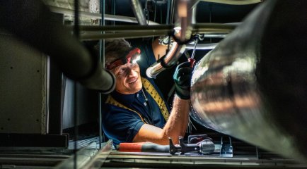 Nærbilde av rørlegger som utfører kontroll på teknisk anlegg med hodelykt